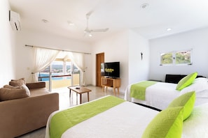 Ein Hotelzimmer mit zwei Betten, einem Sofa, einem Fernseher und einem Balkon mit Blick.