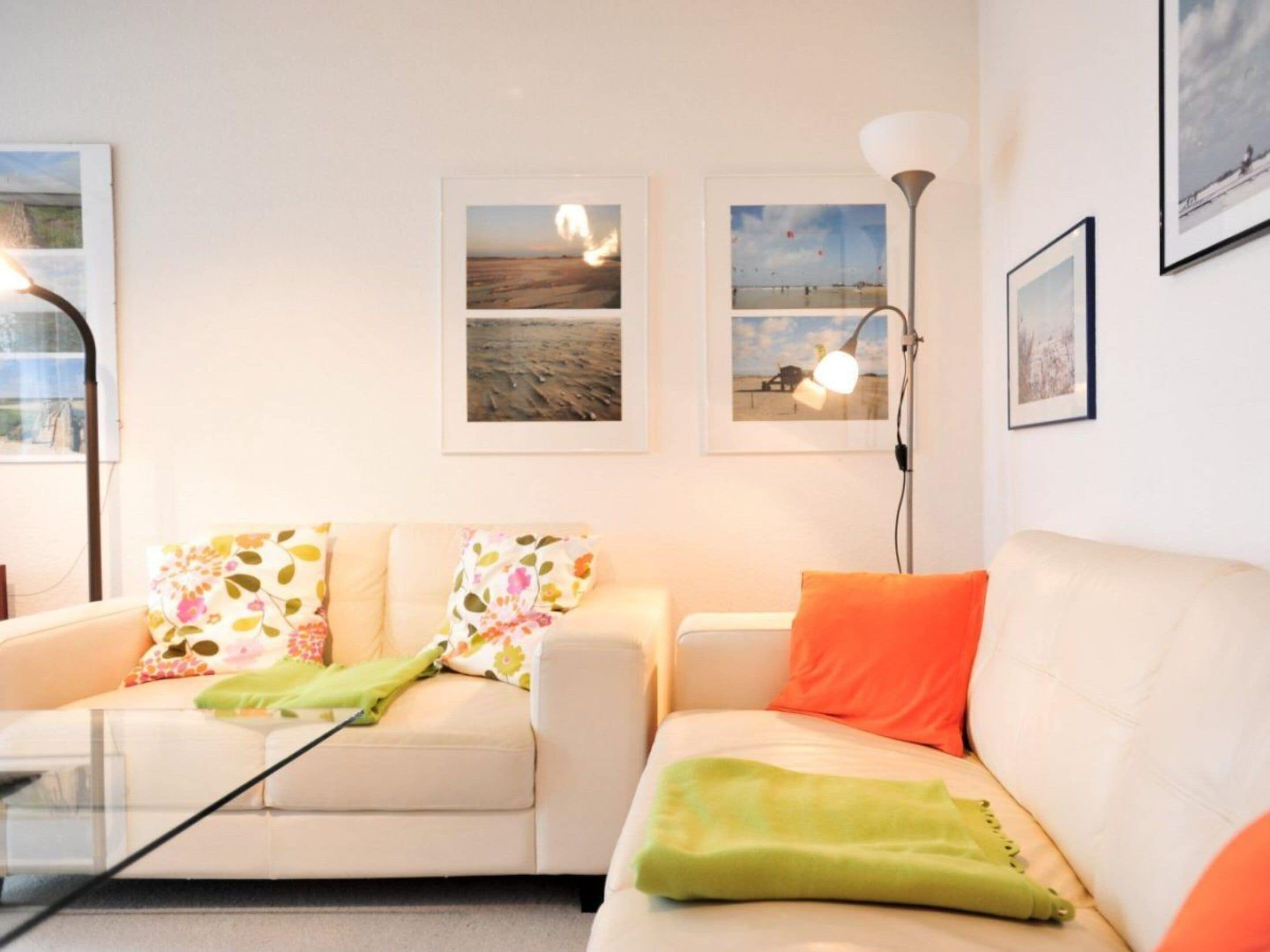 Een woonkamer met een bank, een salontafel en een vloerlamp. Drie ingelijste foto's hangen aan de muur.