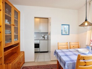 A compact kitchen with white cabinets, a coffee maker, and a dining area with a table and chairs. - 11 in the House at Blanker-hans-weg 5 (St. Peter-Ording)