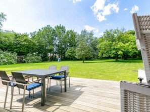 Eine Terrasse mit Tisch und Stühlen, umgeben von einer grünen Wiese und Bäumen.