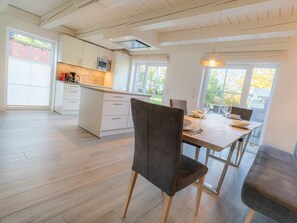 Eine moderne Küche mit weißen Schränken, einer zentralen Kochinsel und einem Essbereich mit Holztisch und Stühlen.