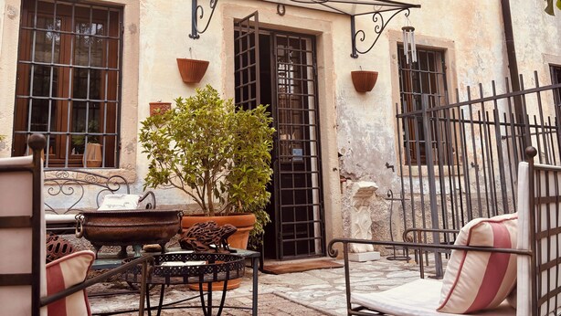 A courtyard with outdoor seating, a wrought iron gate, and a building with green shutters. - Vrbo Property (Cison di Valmarino)