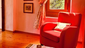 A room with a red armchair, a wooden table with a teapot and a cup, and three framed pictures on the wall. - Vrbo Property (Cison di Valmarino)