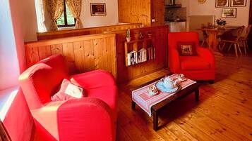 Ein gemütliches Wohnzimmer mit einem roten Sofa, einem Couchtisch aus Holz mit einem Teekessel und einem Bücherregal.