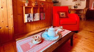 Una stanza accogliente con pareti in legno, una poltrona rossa, un tavolo in legno con un servizio da tè e una libreria piena di libri.