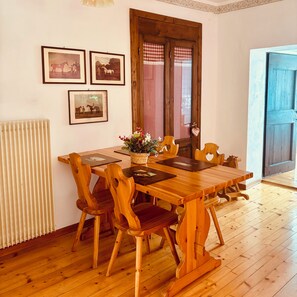 Een houten eettafel met stoelen, een radiator en ingelijste foto's aan de muur.
