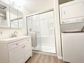 A modern bathroom with a glass shower enclosure, a white sink with a mirror, and a built-in washing machine. - Private Entrance Mini Studio S/AC/Laundry/Wifi (El Monte)