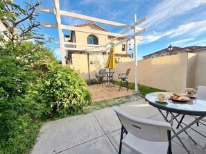 A patio area with a table and chairs, a yellow umbrella, and a view of a building in the background.