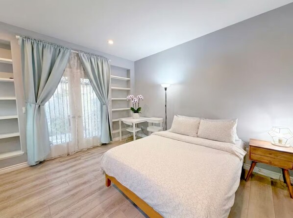 A bedroom with a bed, a bedside table, a lamp, and a window with curtains.