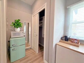 A compact kitchen with a microwave, a small refrigerator, and a window with blinds.