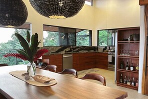 Cozinha moderna com mesa de jantar de madeira, adega embutida e grandes janelas com vista para o exterior.
