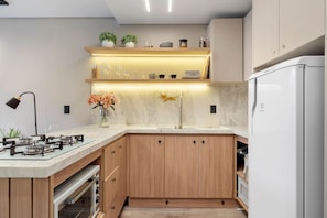 A modern kitchen with a gas stove, a built-in oven, a sink, and a refrigerator. - Apto YOU 206 (Canela)