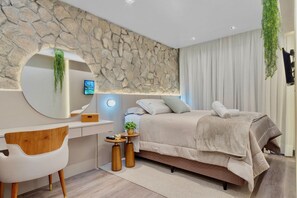 Un dormitorio moderno con una pared de piedra, una cama con cubrecama acolchado, una mesita de noche con una planta, un espejo redondo y un televisor montado en la pared.