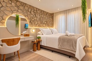 Un dormitorio moderno con una pared de acento de piedra, una cama con ropa de cama blanca, un escritorio con una silla y un televisor montado en la pared.