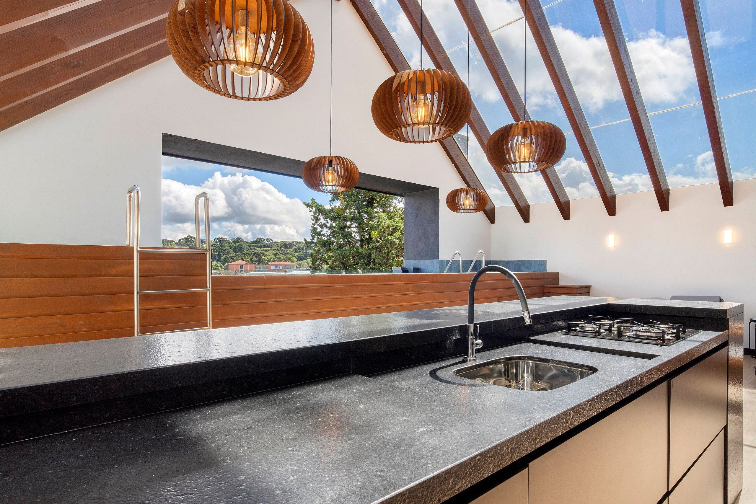 Cozinha moderna com ilha grande, pia de aço inoxidável e detalhes em madeira.