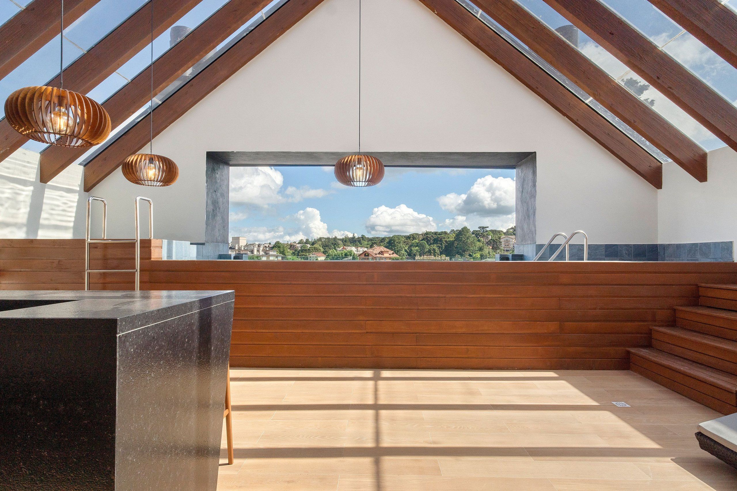 Um interior moderno com uma janela ampla, vigas de madeira e dois luminários suspensos.