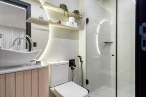 Un baño moderno con un lavamanos blanco grande, un inodoro y una zona de ducha con mampara de vidrio.