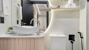 A modern bathroom with a large white vessel sink, a toilet, and a shower area. - Apto YOU 206 (Canela)