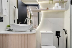 A modern bathroom with a large white vessel sink, a toilet, and a shower area. - Apto YOU 206 (Canela)