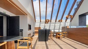 A modern kitchen with a central island, wooden chairs, and a dining area with a view of the sky. - Apto YOU 206 (Canela)