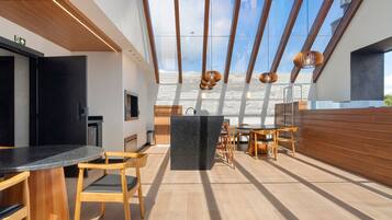 Cocina moderna con isla central, sillas de madera y comedor con vistas al cielo.