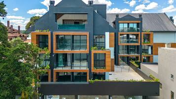 A modern multi-story building with large windows, balconies with greenery, and a visible commercial space on the ground floor.