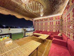 A rooftop lounge with patterned walls, red seating, and a view of the cityscape. - Oscar Pyramids view (Giza)