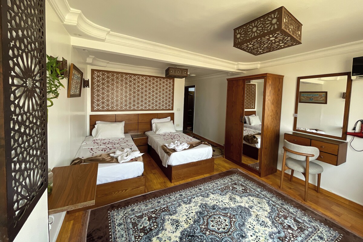 A hotel room with two beds, a wooden wardrobe, a mirror, and a patterned rug.
