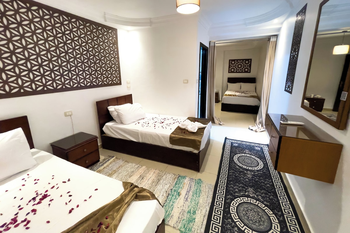 A hotel room with two beds, a large decorative wall panel, a mirror, and a patterned rug.
