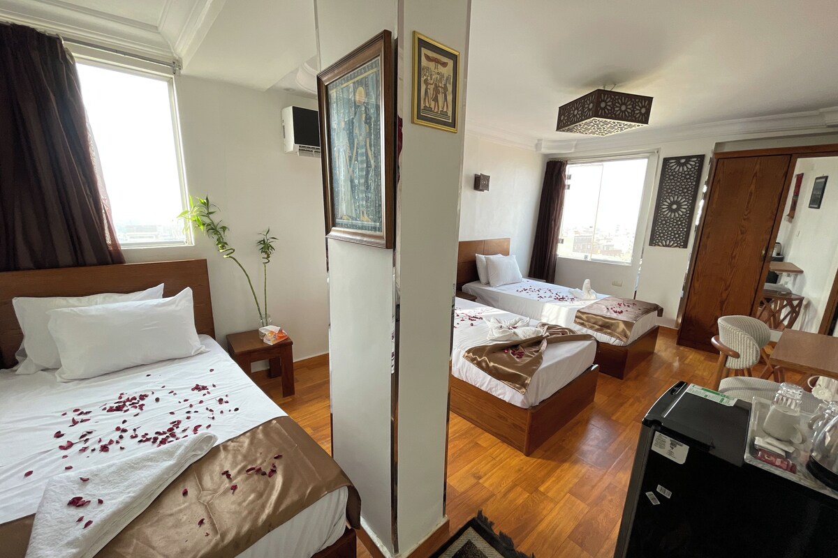 A hotel room with two beds, a desk, a refrigerator, and a window with curtains.