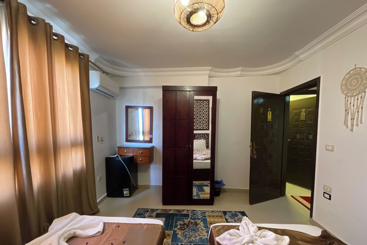 A hotel room with a bed, a desk, a wardrobe, and a door leading to another room.