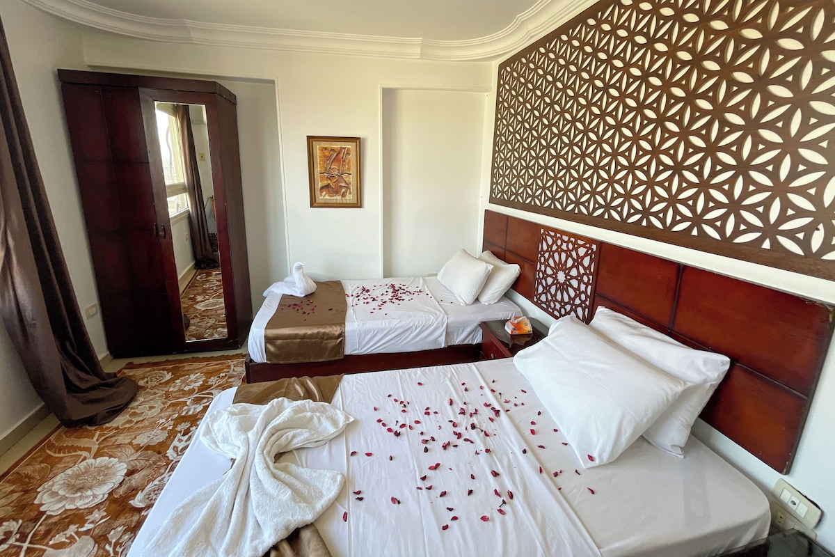 A hotel room with two beds, a decorative wall panel, a framed picture, and a carpeted floor.