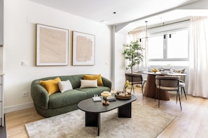 Ein stilvolles Wohnzimmer mit einem grünen Sofa, einem Couchtisch und einem Essbereich mit Holztisch und Stühlen.