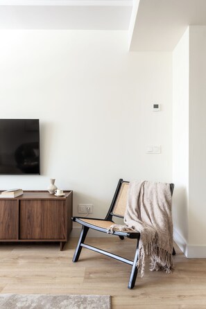 Ein modernes Wohnzimmer mit Holzboden, einem schwarzen Stuhl mit Gewebesitz, einem Holztisch, einem flachbildfernseher an der Wand und einer weißen Wand mit Steckdose.
