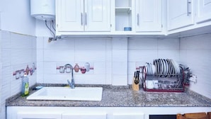 A kitchen with white cabinets, a granite countertop, a sink, a dish rack, and a water heater. - EDEN GARDEN LUXURIOUS GUEST HOUSE (Yaoundé)