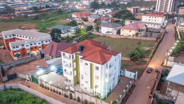 A multi-story building with a parking area and a road in front. - EDEN GARDEN LUXURIOUS GUEST HOUSE (Yaoundé)