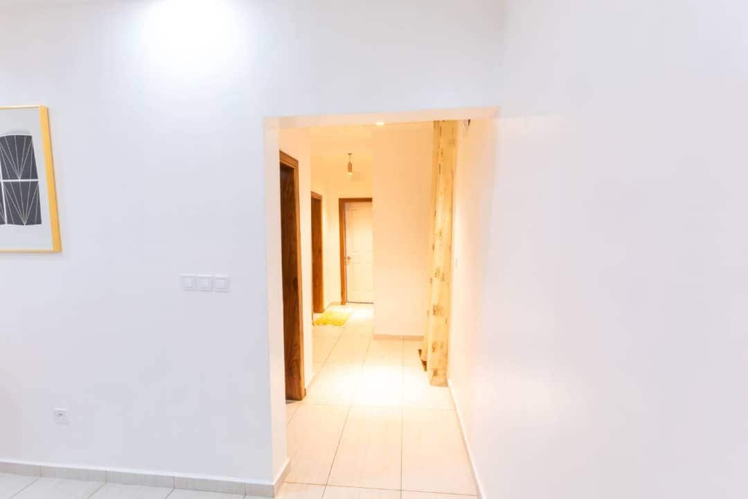 Un pasillo con una puerta que da a otra habitación, un interruptor de luz y un cuadro en la pared.