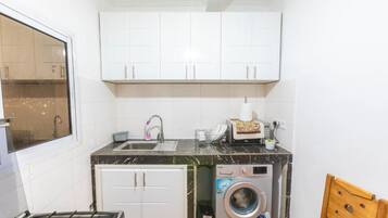 Cocina compacta con armarios blancos, un lavabo, una estufa y lavadora integrada.