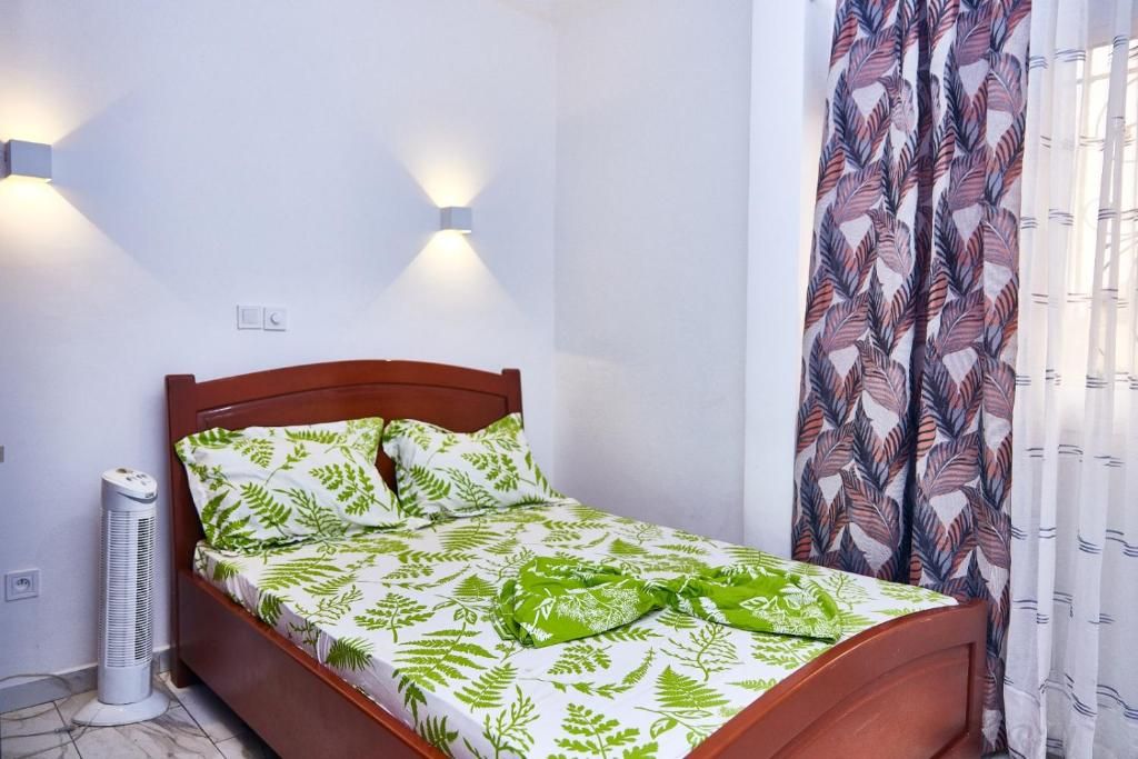 Una cama individual con cabecera de madera, un calentador de pared y una ventana con cortinas estampadas.