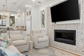 A modern living room with a fireplace, a large flat-screen TV mounted on the wall, and a seating area with two armchairs. - New to Rental Market! Located in Prestigious Carillon Beach! (Panama City Beach)