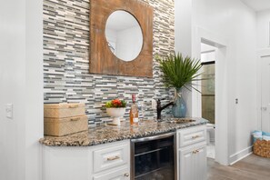 A kitchen with a granite countertop, white cabinetry, a wooden backsplash, and a mirror above the sink. - New to Rental Market! Located in Prestigious Carillon Beach! (Panama City Beach)