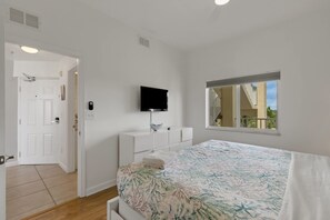 Ein Schlafzimmer mit einem Bett, einem an der Wand montierten Fernseher, einem Fenster mit Blick und einer Tür zu einem anderen Raum.