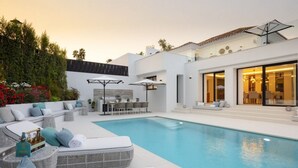 A modern outdoor pool area with a lounge, dining area, and a large windowed room. - Vrbo Property (Marbella)