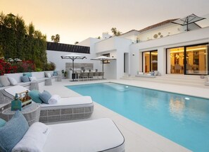 Ein moderner Poolbereich im Freien mit Lounge-Bereich, Essbereich und einem großzügigen Raum mit Panoramafenstern.