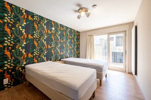 A hotel room with two beds, a ceiling fan, and a large window with curtains. - Apartment in Blankenberge With Sea View (Blankenberge)