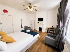 Ein Hotelzimmer mit Bett, Sessel, Fernseher, Kamin und Deckenventilator.