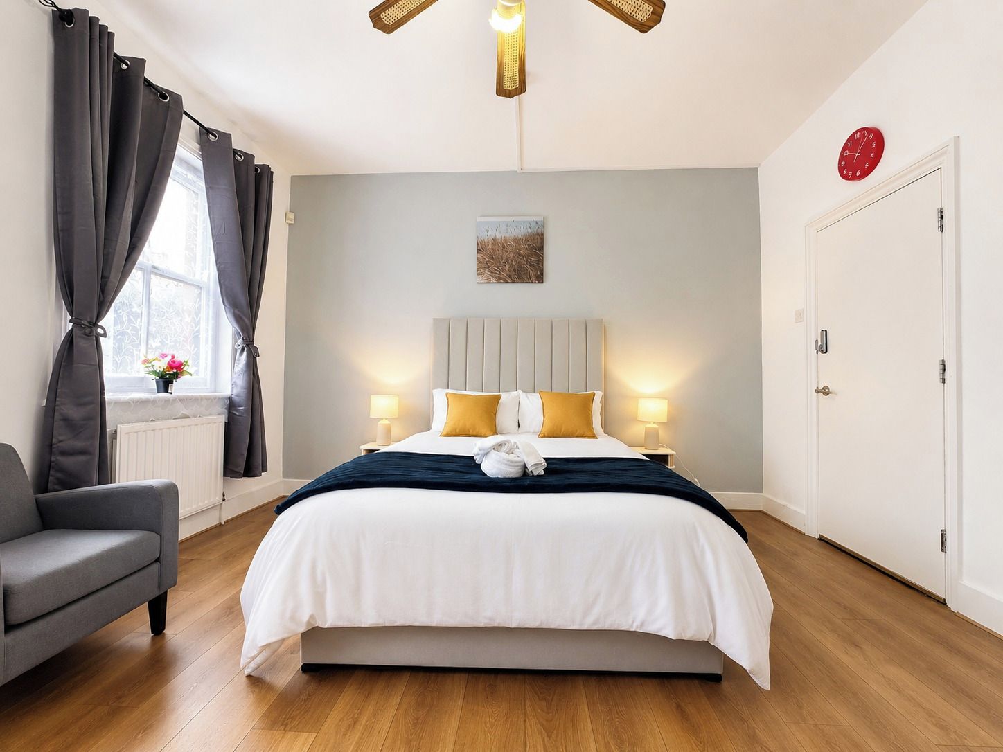 Una habitación de hotel con cama, lámparas de noche, una ventana con cortinas, un radiador, un sofá y una puerta.