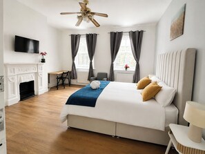 Ein Hotelzimmer mit einem Bett, einem Schreibtisch, einem Sessel, einem Kamin, einem Fernseher und einem Deckenventilator.