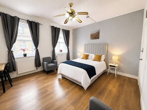 Ein Hotelzimmer mit einem Bett, einem Sessel, einem Schreibtisch, einer Stehlampe und einem Deckenventilator.