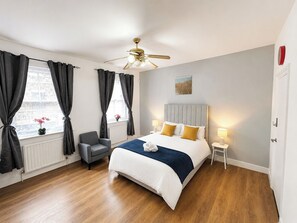 Ein Hotelzimmer mit einem Bett, einem Sessel, einem Deckenventilator und einem Fenster mit Vorhängen.